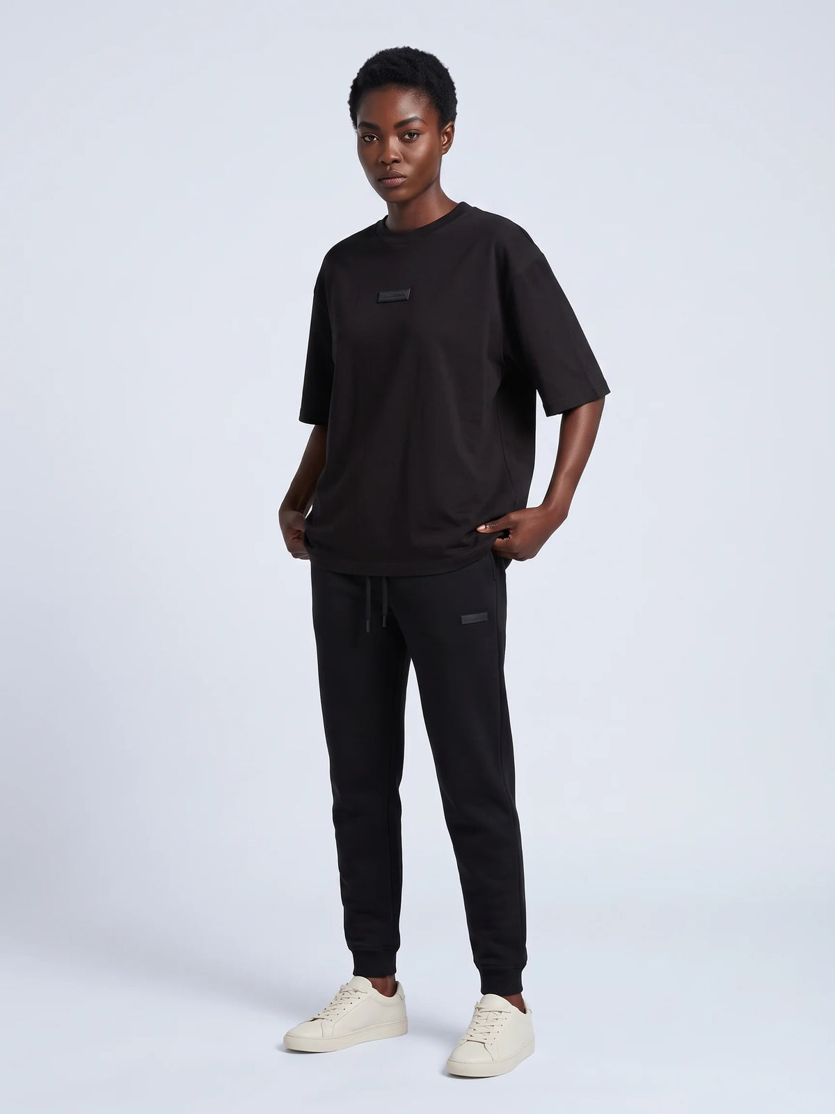 Black organic cotton t-shirt, Unidentity Identity Tee, full-length front view with tonal 3D chest patch and black Core joggers, from Dubai #color_black
