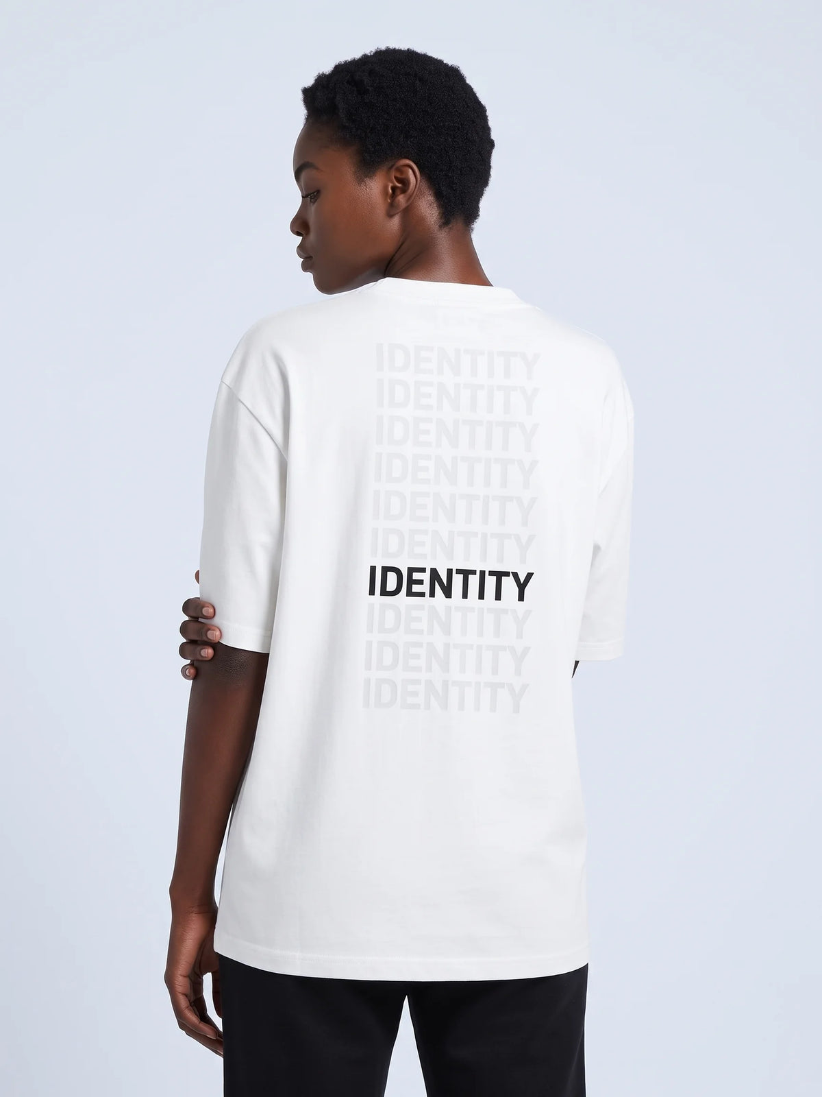 White oversized t-shirt, Unidentity Identity Oversized Tee, back close-up of the fading IDENTITY typographic print worn by woman, sustainable fashion #color_white