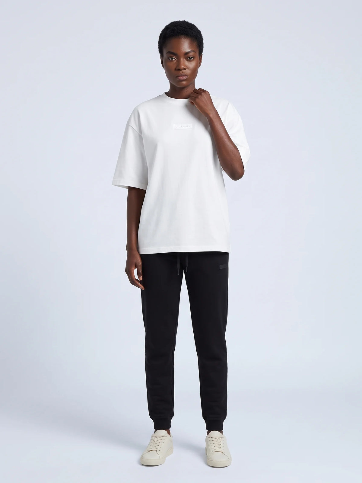 White oversized t-shirt in organic cotton, Unidentity Identity Tee, full-length front view of the crew neck worn by woman, hand at collar, 210gsm #color_white