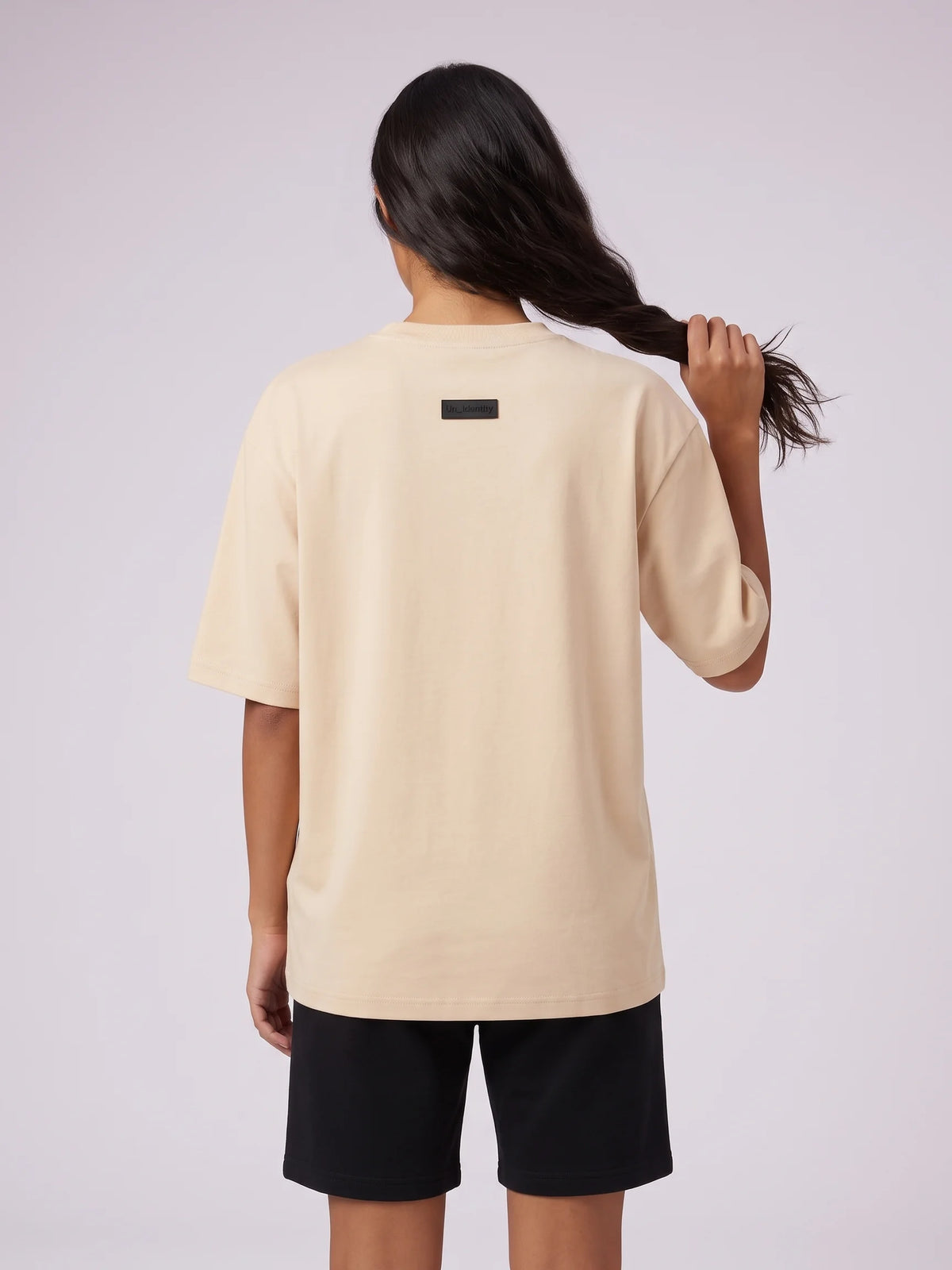 Beige heavyweight oversized t-shirt in organic cotton, Unidentity Foundation Tee, back close-up of the black 3D patch on a woman, UAE streetwear #color_beige