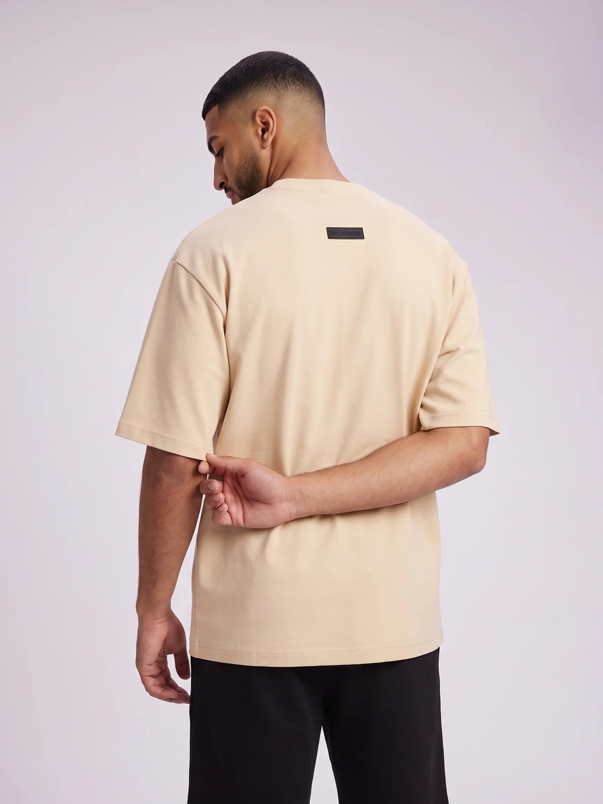 Beige oversized t-shirt, Unidentity Foundation Oversized Tee, upper back view worn by man showing the subtle black 3D patch, sustainable streetwear #color_beige
