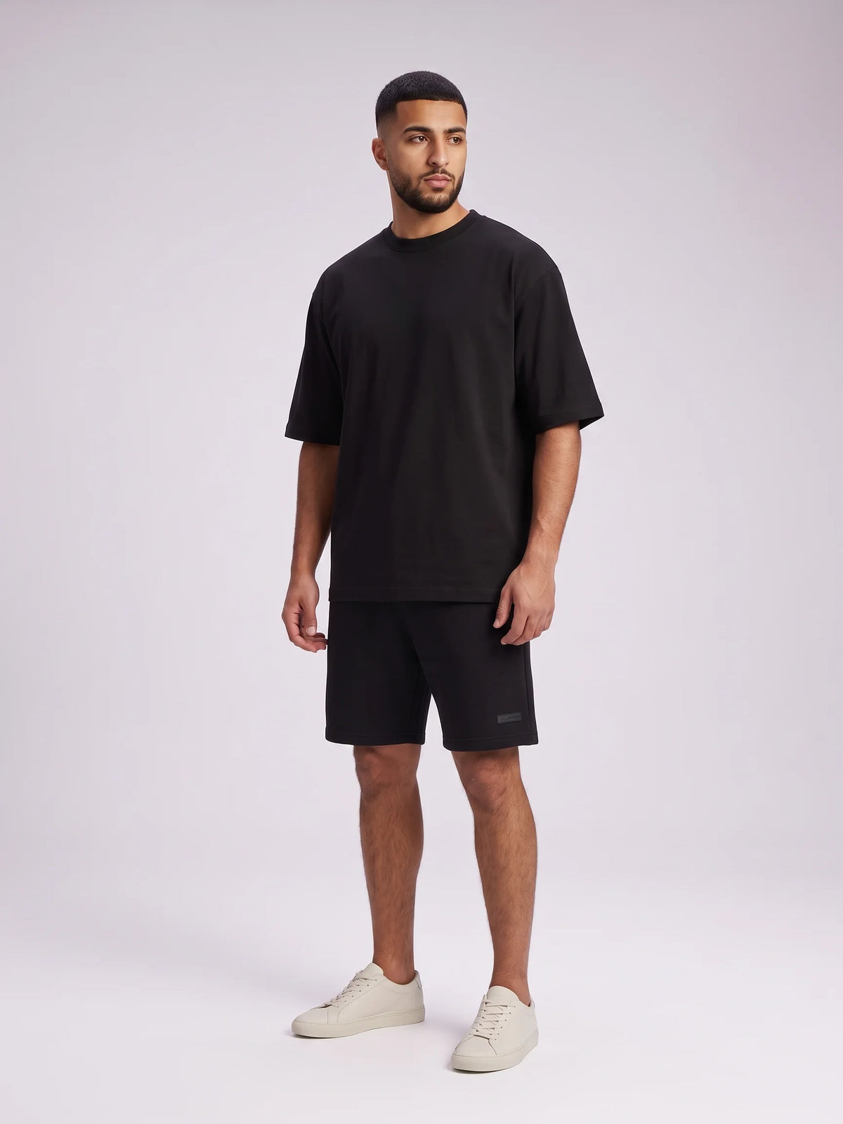 Black oversized t-shirt in organic cotton, Unidentity Foundation Tee, full-length front view worn by man with black shorts, streetwear from Dubai #color_black