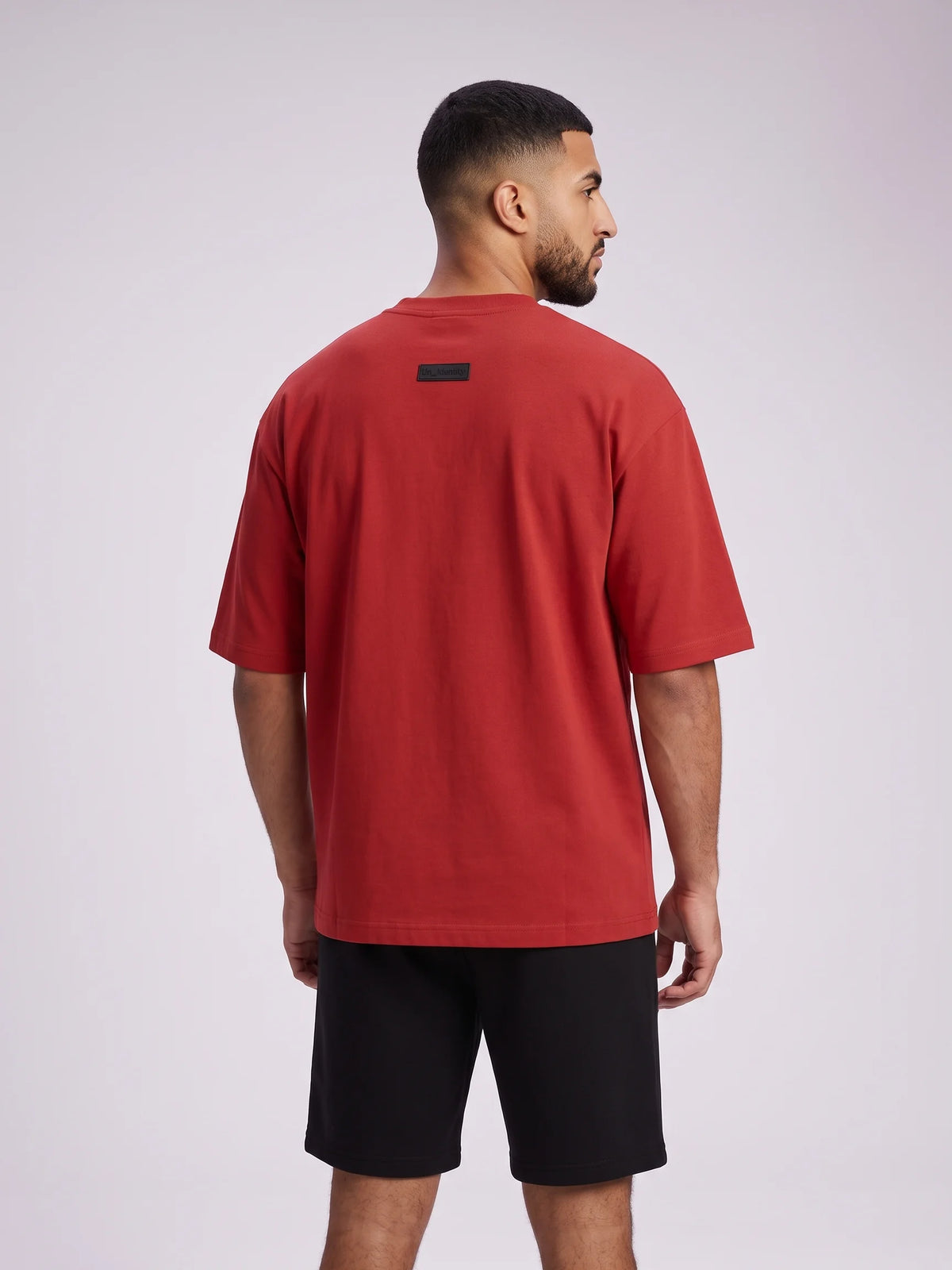 Red oversized t-shirt, Unidentity Foundation Oversized Tee, upper back view worn by man showing the boxy cut and black 3D patch, streetwear #color_red