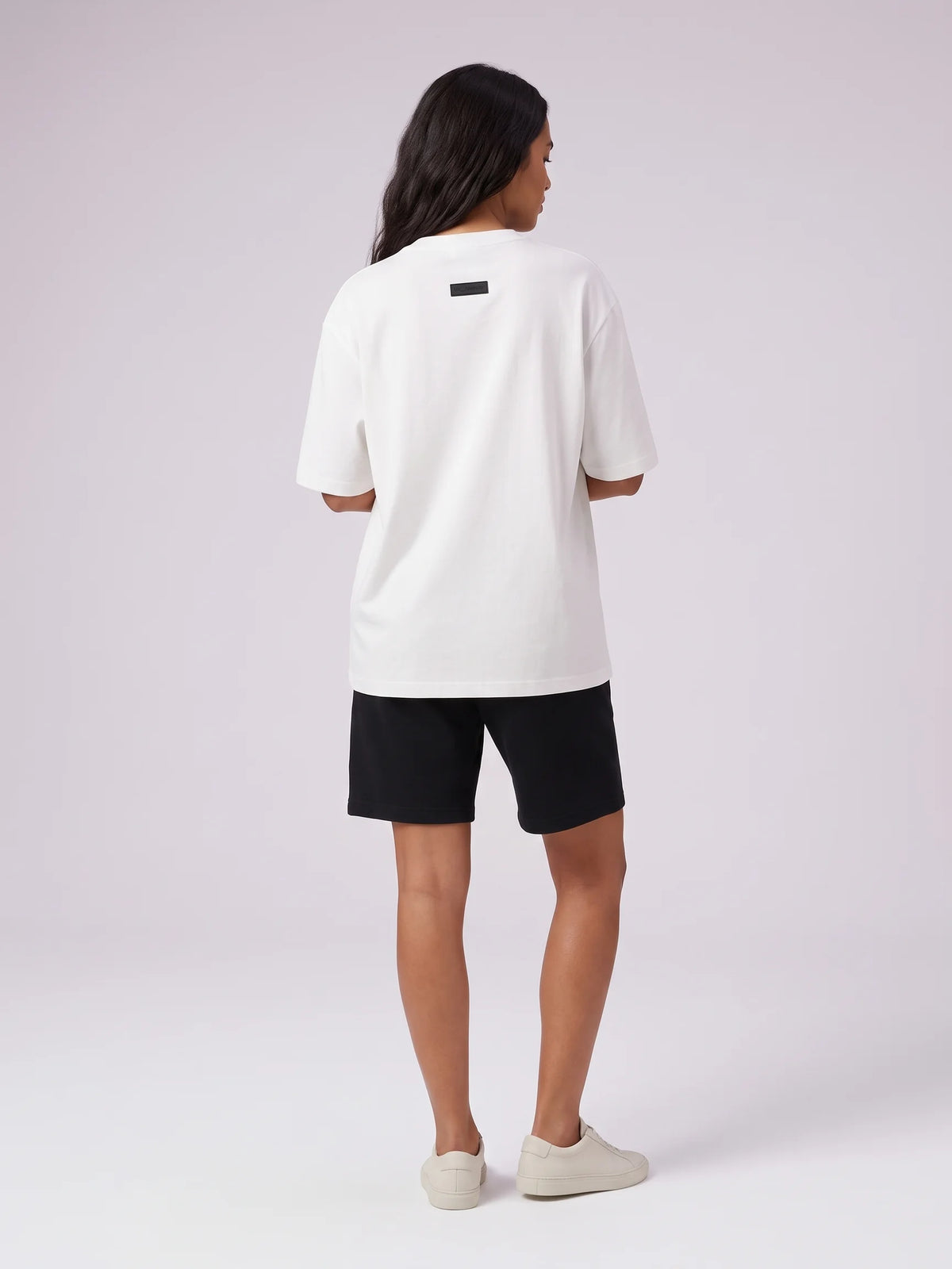 White oversized t-shirt, Unidentity Foundation Oversized Tee, full-length back view worn by woman with black Core shorts, streetwear brand in Dubai #color_white