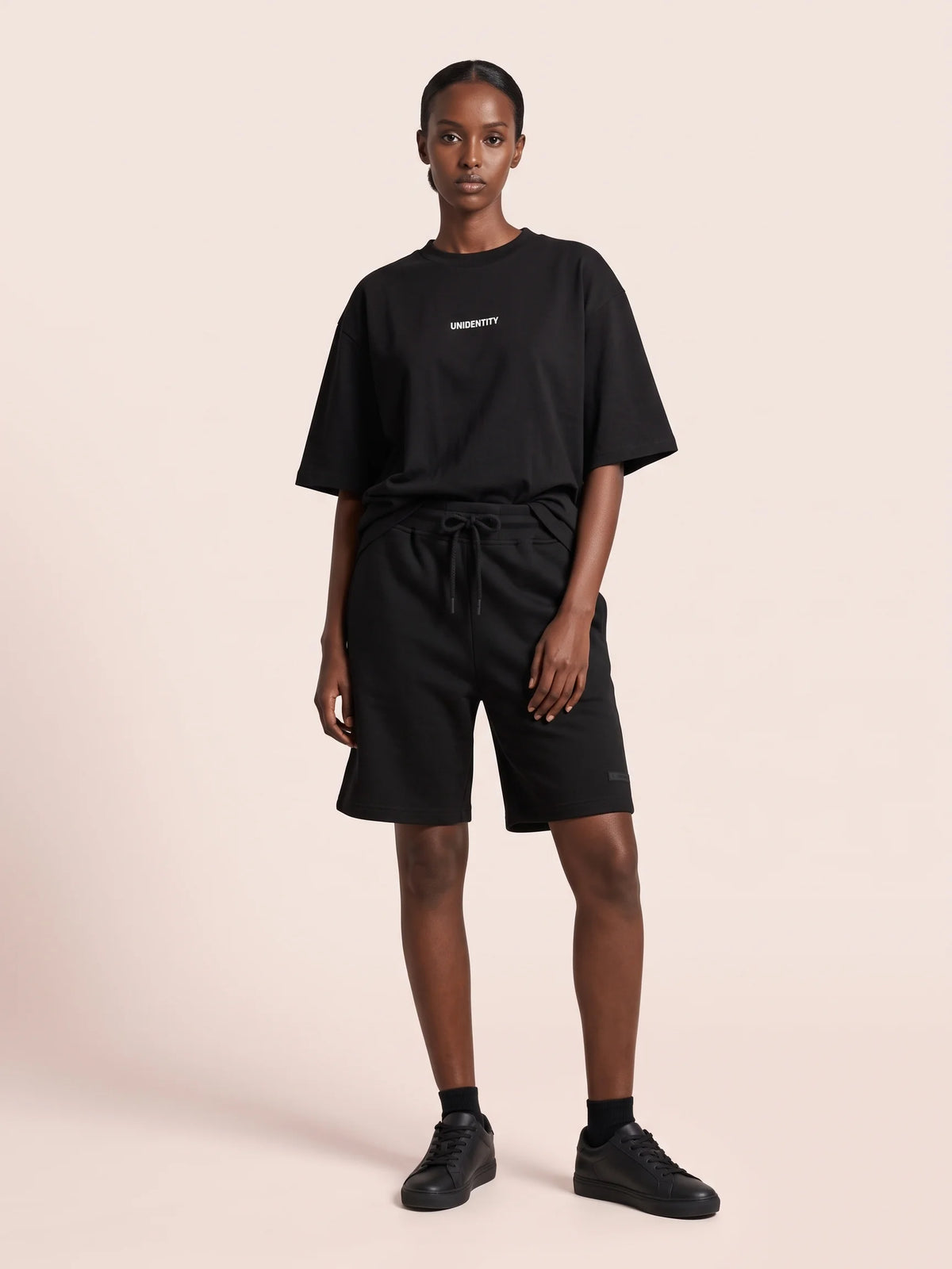 Black organic cotton t-shirt, Unidentity Dare Oversized Tee, full-length front view with white chest logo, styled with black Core shorts #color_black