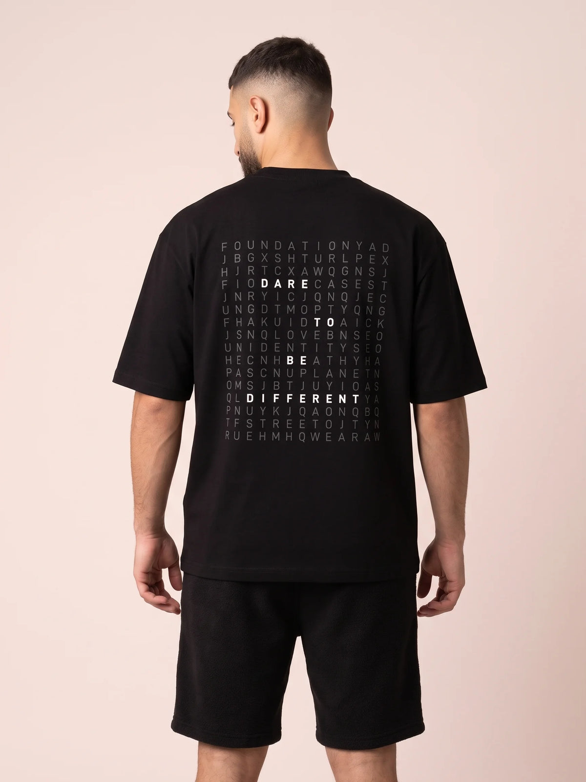 Black oversized t-shirt, Unidentity Dare Tee, close back view worn by man showing the gray and white word search print, sustainable streetwear #color_black