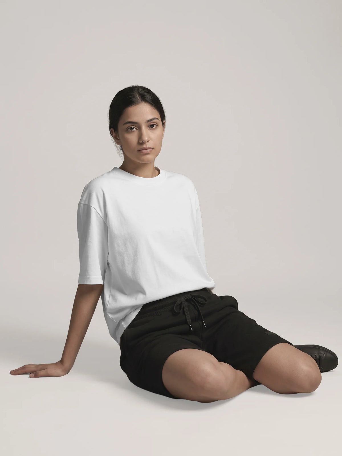 White oversized t-shirt, Unidentity You Tee, front view of a woman seated on the floor in black Core shorts, streetwear from the UAE #color_white