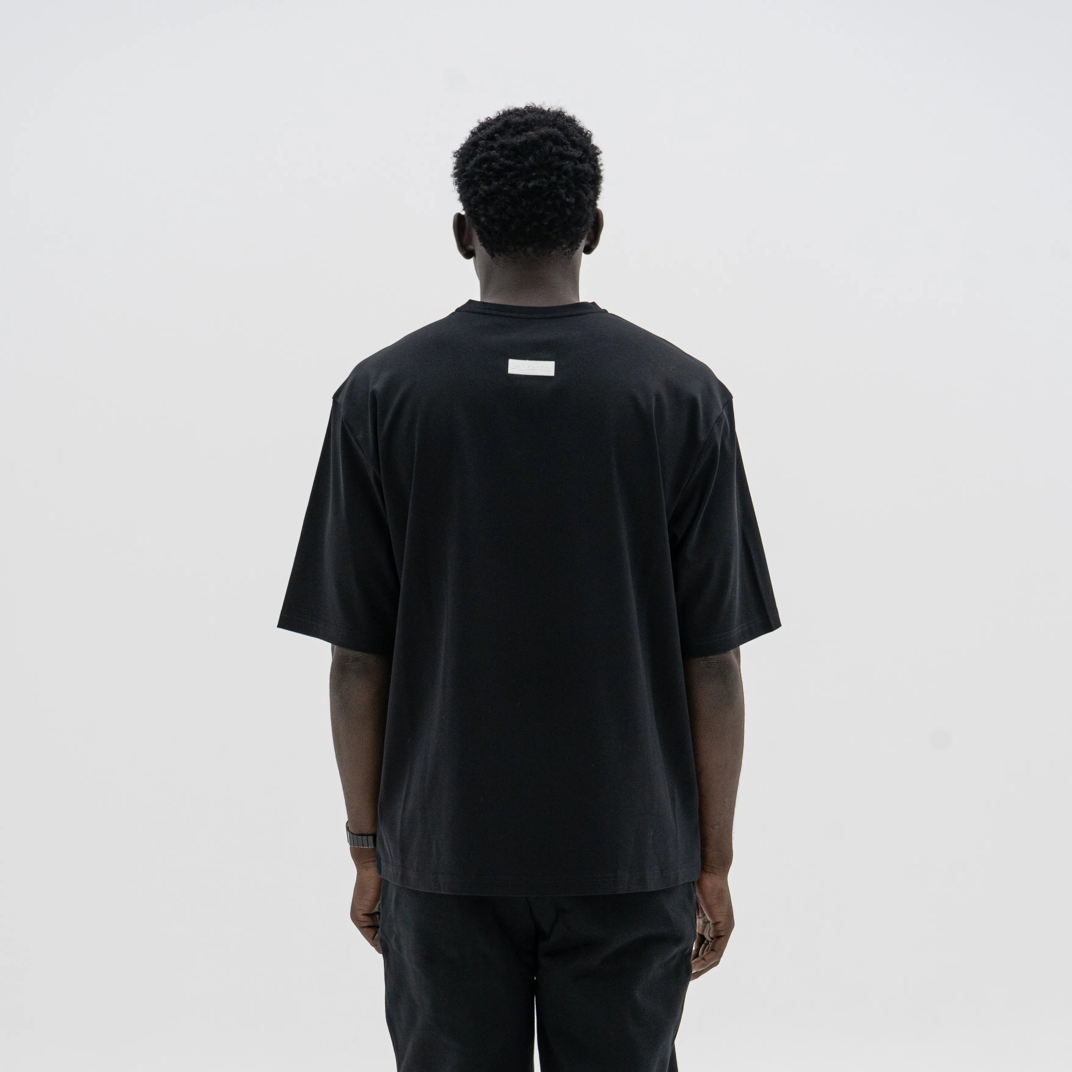 Person wearing a black t-shirt with a small white logo on the back against a plain background. #color_black