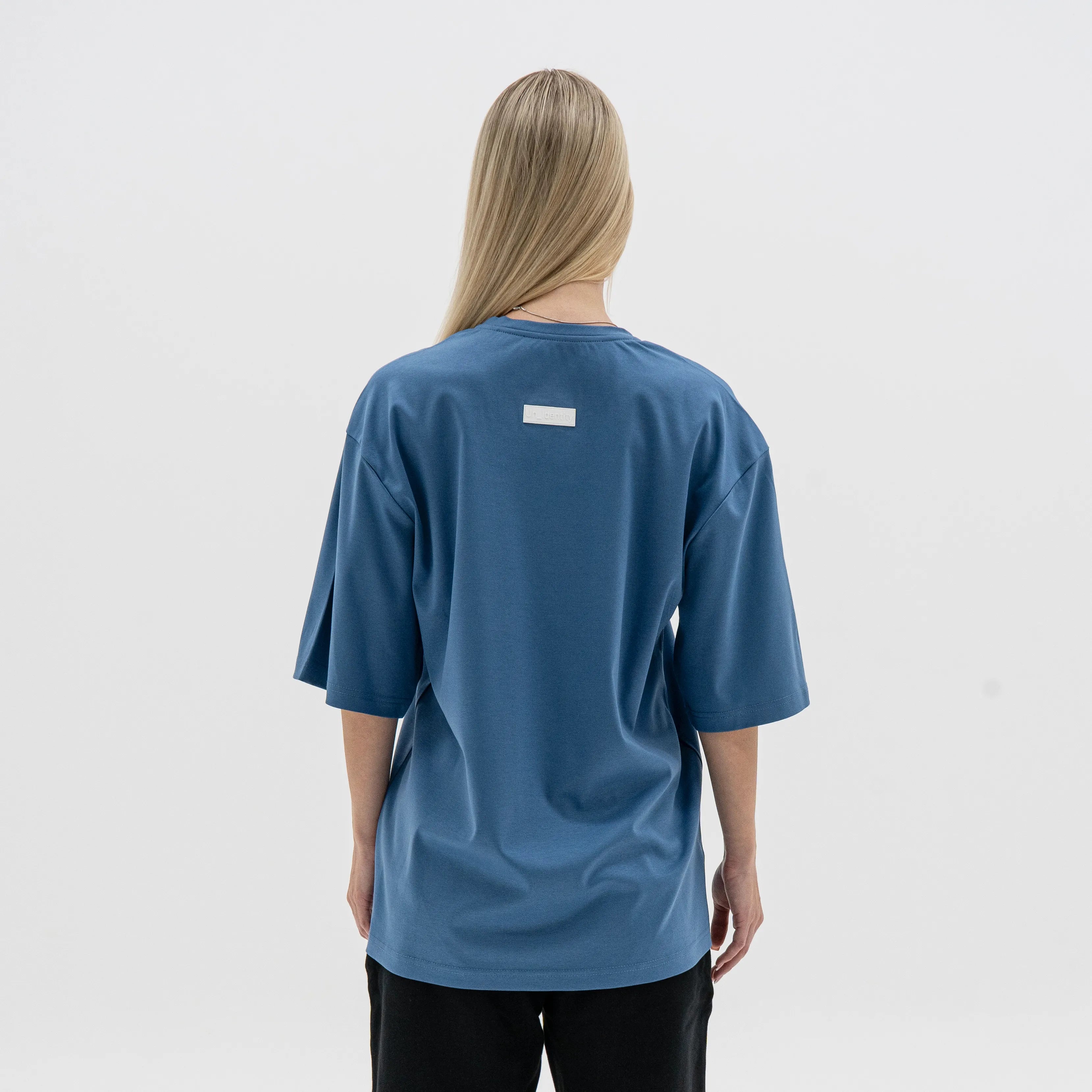 Person wearing a blue t-shirt with a small white logo on the back against a plain background. #color_blue