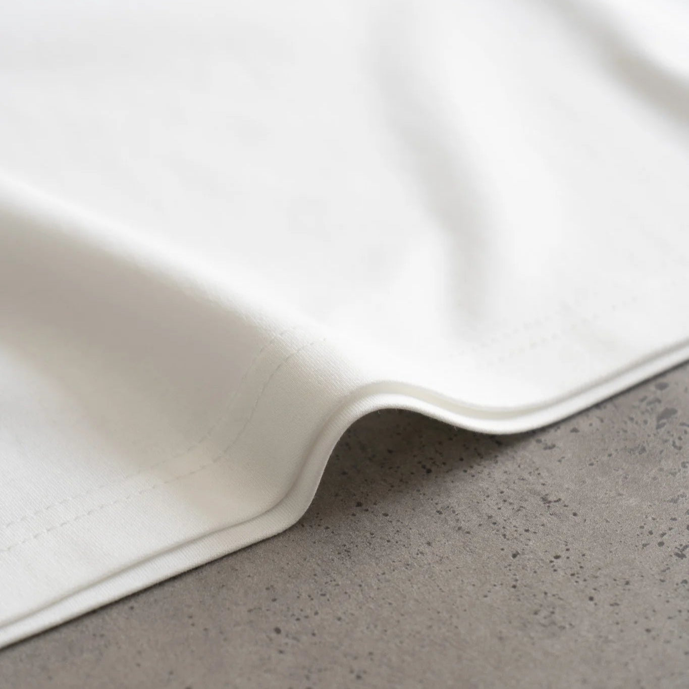 White t-shirt detail on a gray concrete surface. #color_white