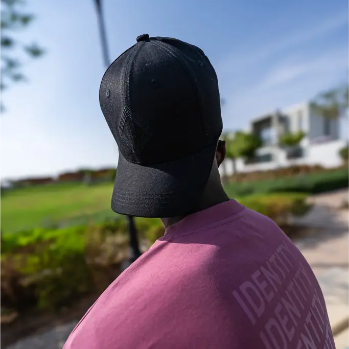 Person wearing black baseball cap and maroon T-shirt with Identity text, standing outdoors 