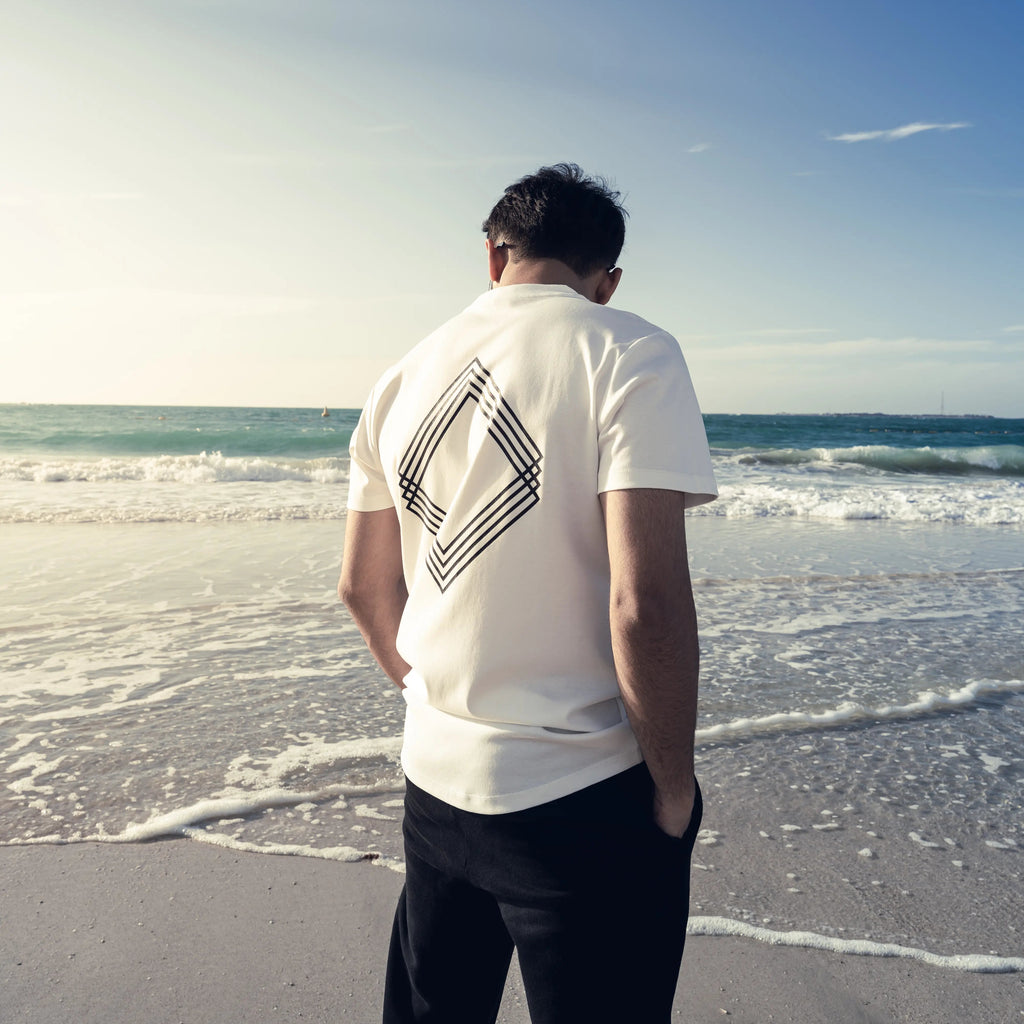 Man looking at the ocean wearing white tee featuring black geometric Unidentity logo 