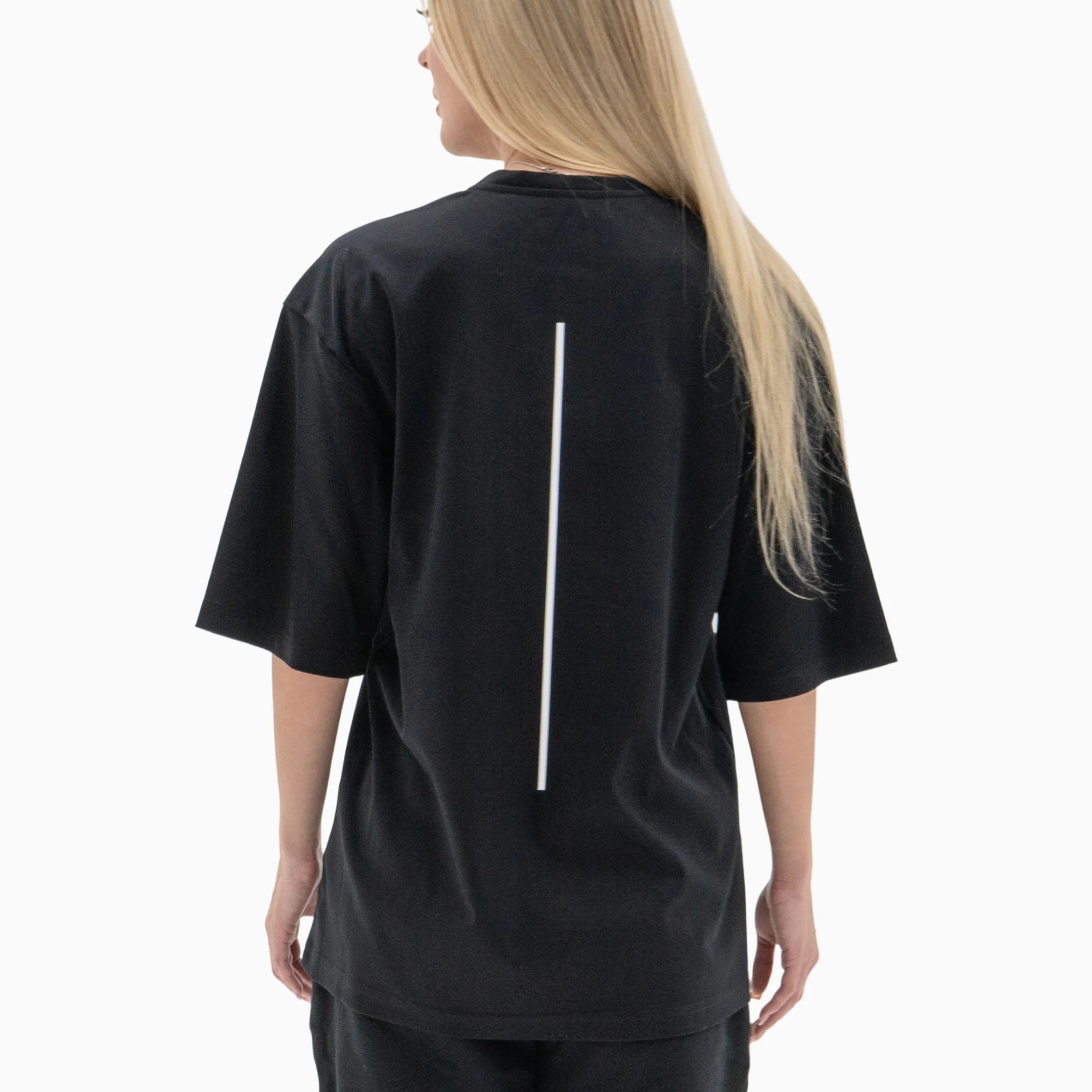 Person wearing a black t-shirt with a white line on the back against a plain background. #color_black