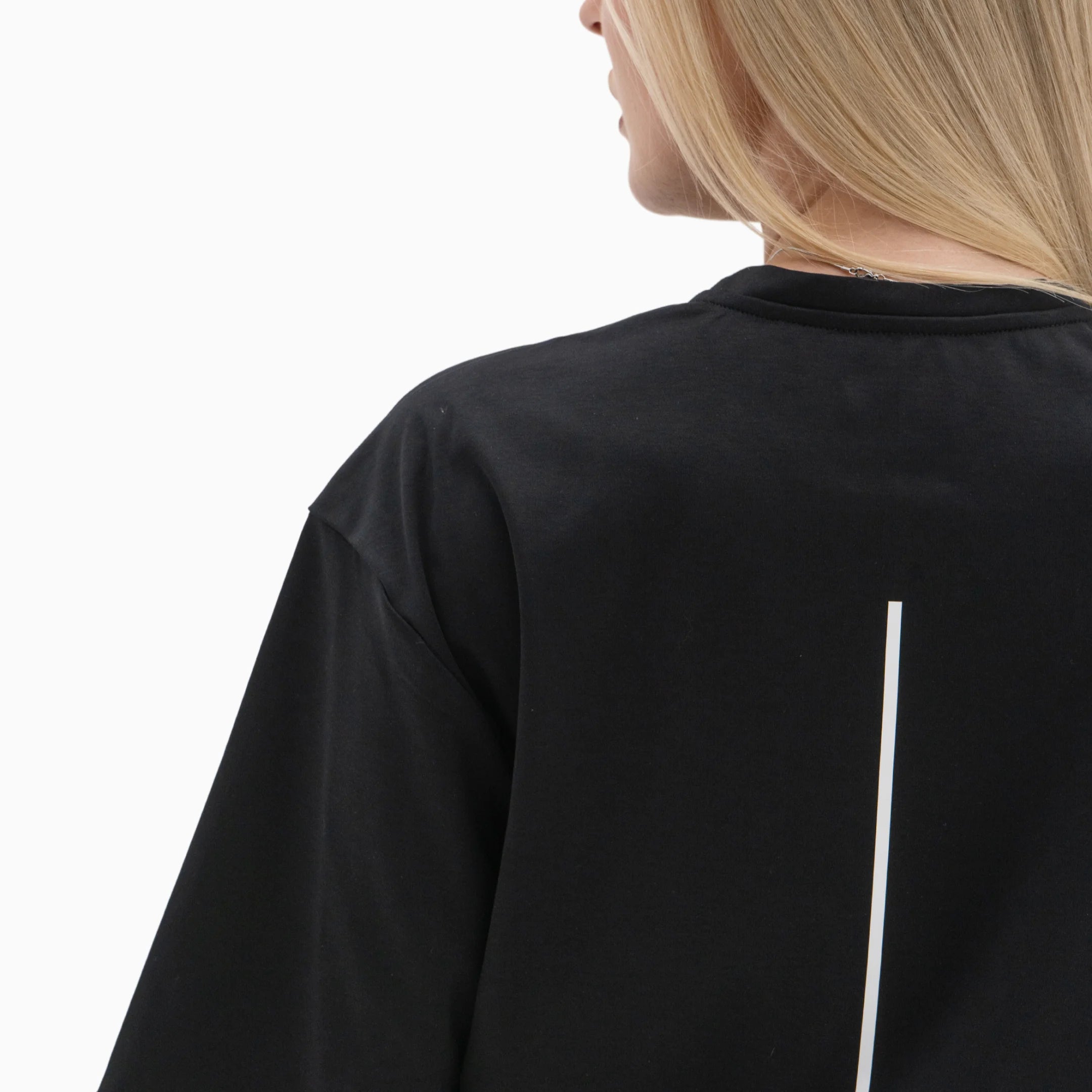 Person wearing a black t-shirt with a white line on the back against a plain background. #color_black