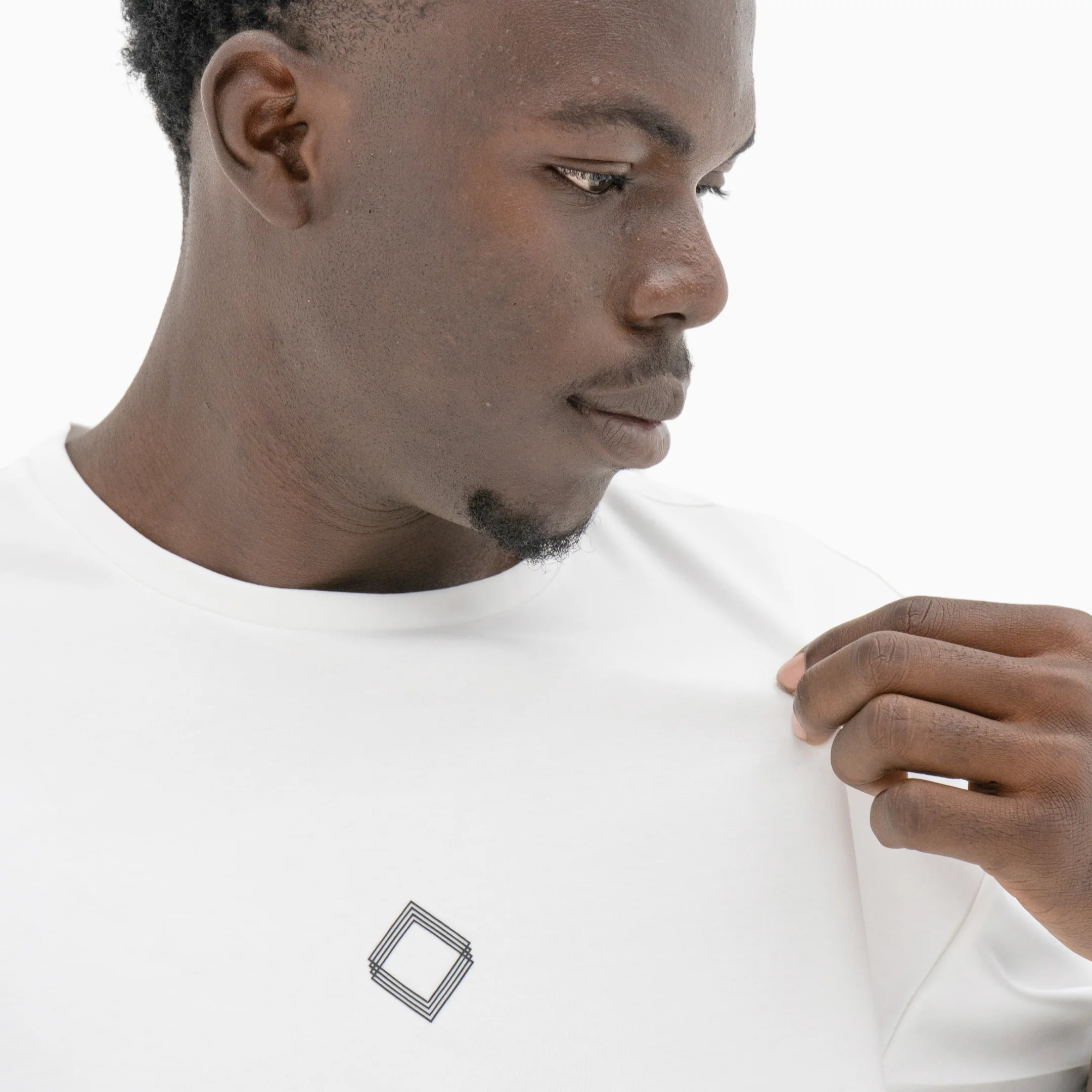 Person wearing a white t-shirt with a black logo on the chest against a plain background. #color_white