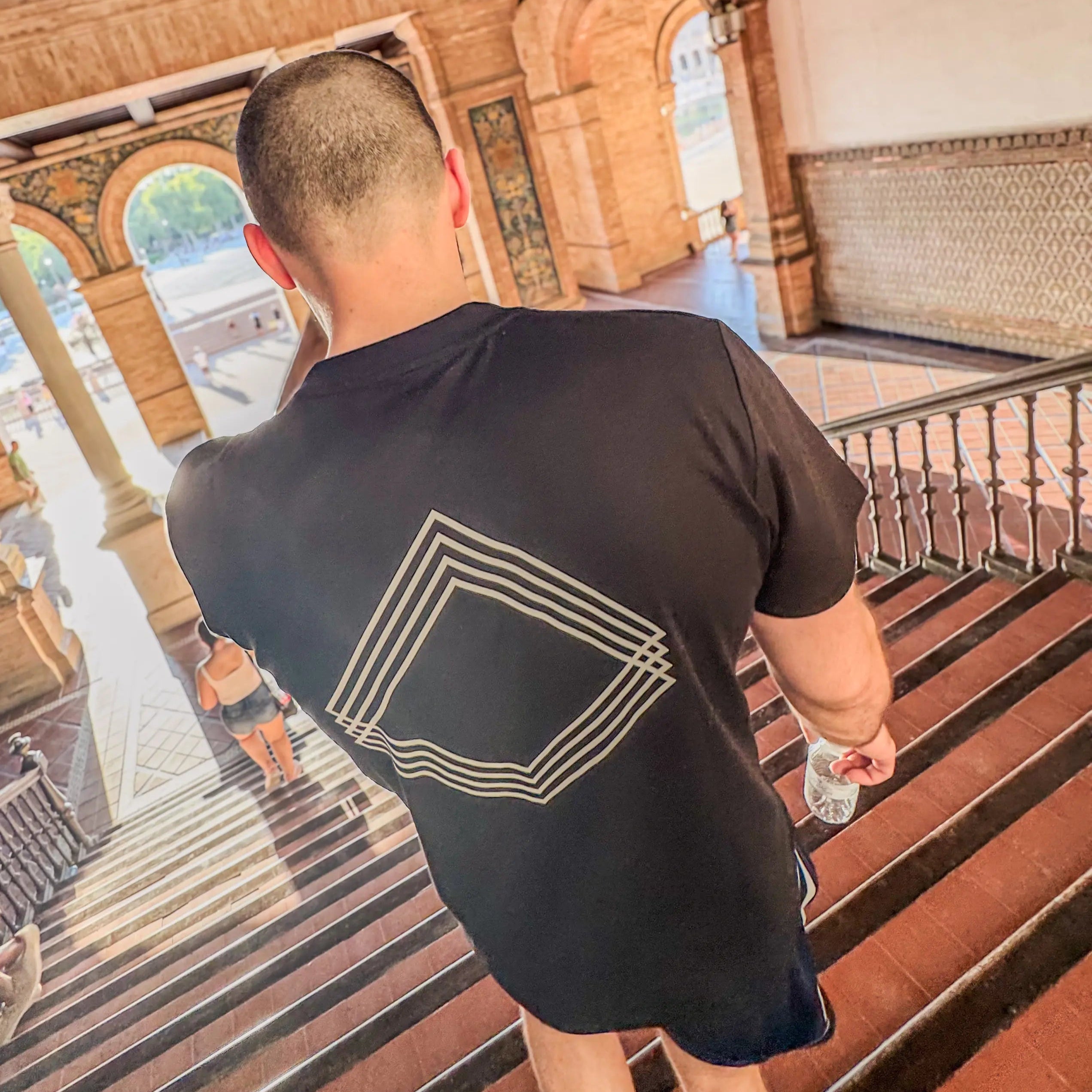 Man wearing black Unidentity T-shirt with geometric white logo on the back going downstairs 