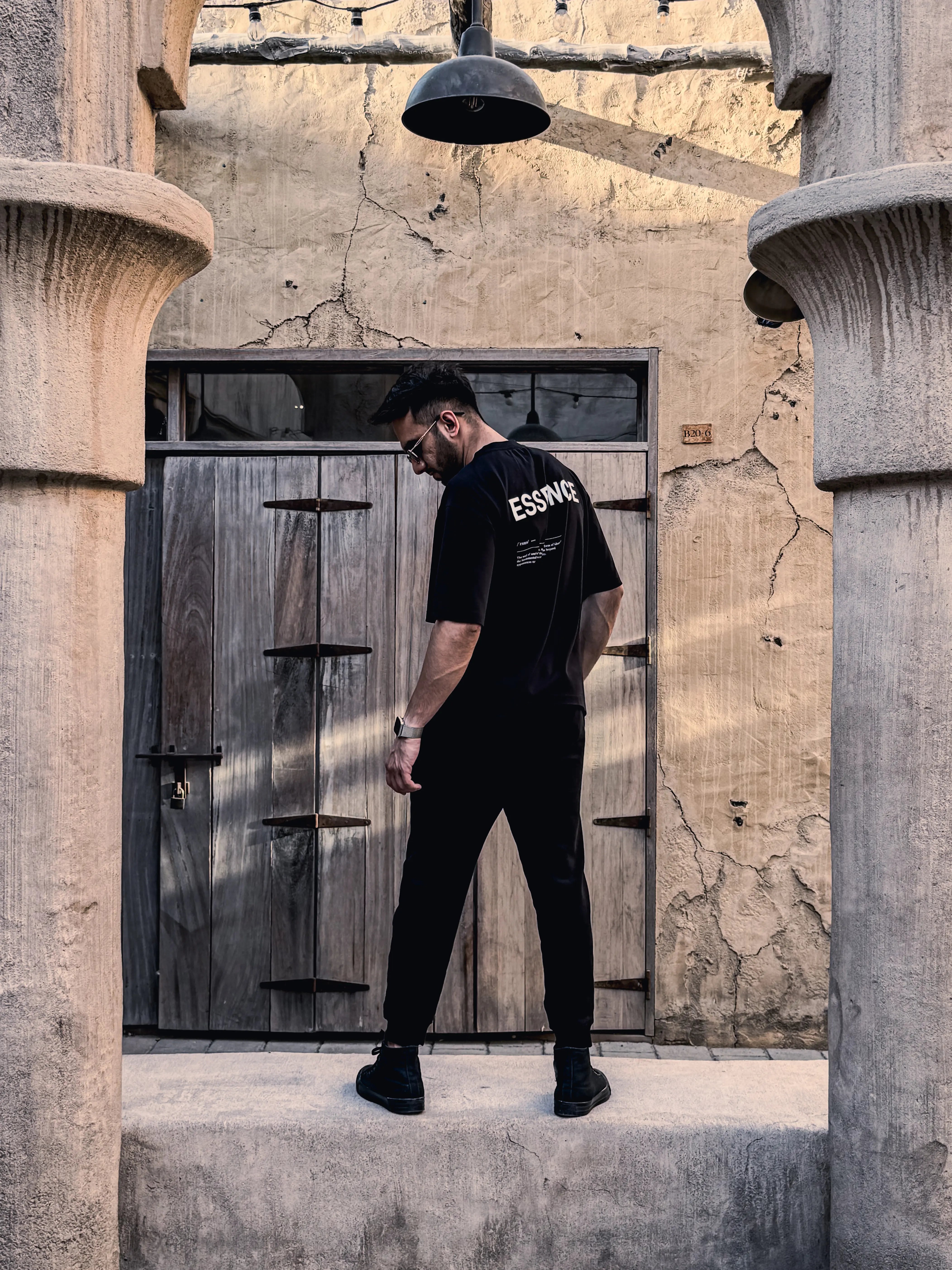 Man in black Unidentity outfit with Essence text standing in an architectural setting. #color_black