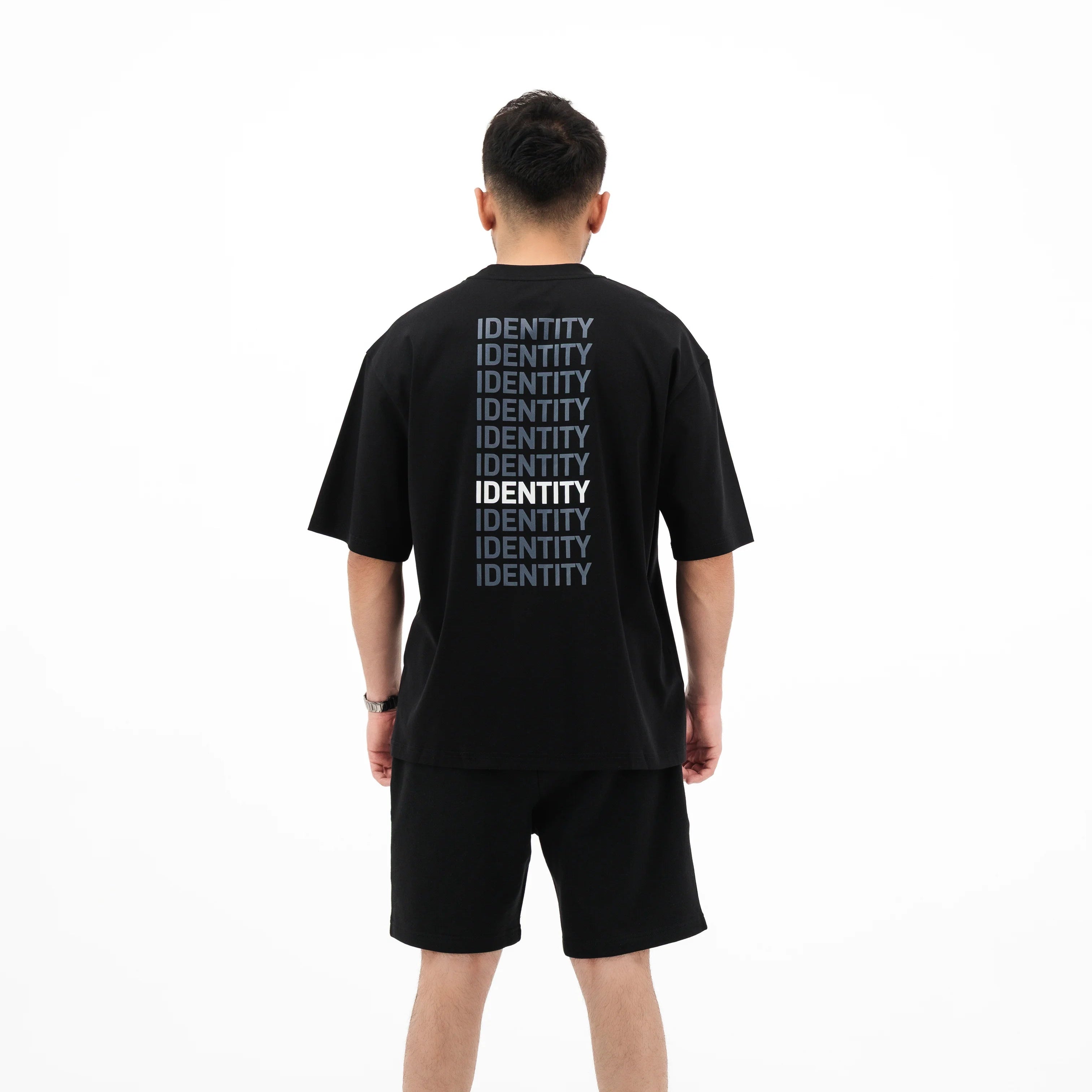 Model wearing black tee with identity text printed multiple times on the back